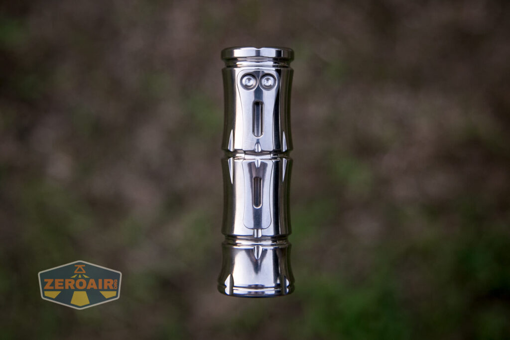 A shiny, metallic cylindrical object with a face-like design stands upright against a blurred brown and green background. The ZeroAir logo is visible in the bottom left corner.