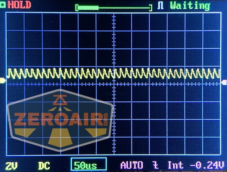 An oscilloscope screen displays a repeating waveform with small oscillations. The settings show 2V per division, DC coupling, 50 microseconds per division, and an average voltage of -0.24V. ZEROAIR is overlaid.