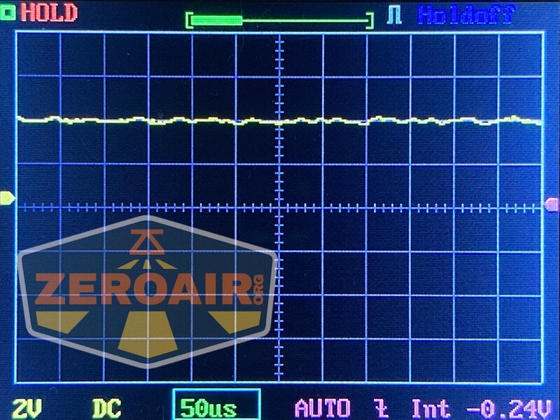 A digital oscilloscope screen displays a mostly flat yellow waveform with minor fluctuations. The settings read 2V per division, 50 microseconds per division, DC mode, and an intensity of -0.24V. Zeroair.org logo overlays the bottom left.