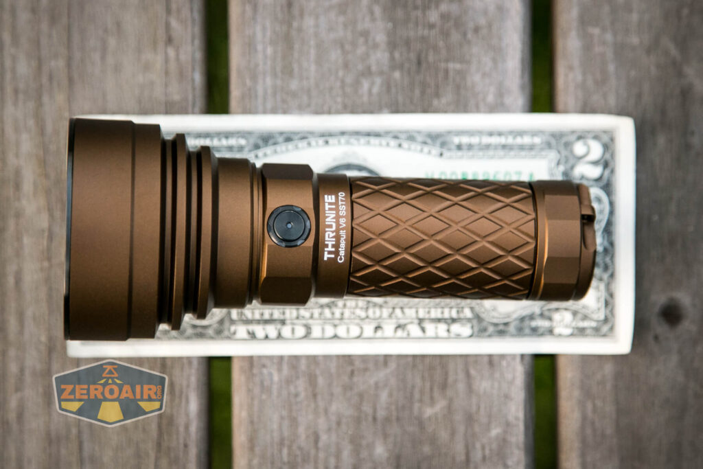 A brown ThruNite flashlight is placed on top of a U.S. two-dollar bill, both resting on a wooden surface. A ZeroAir logo is visible in the lower left corner of the image.