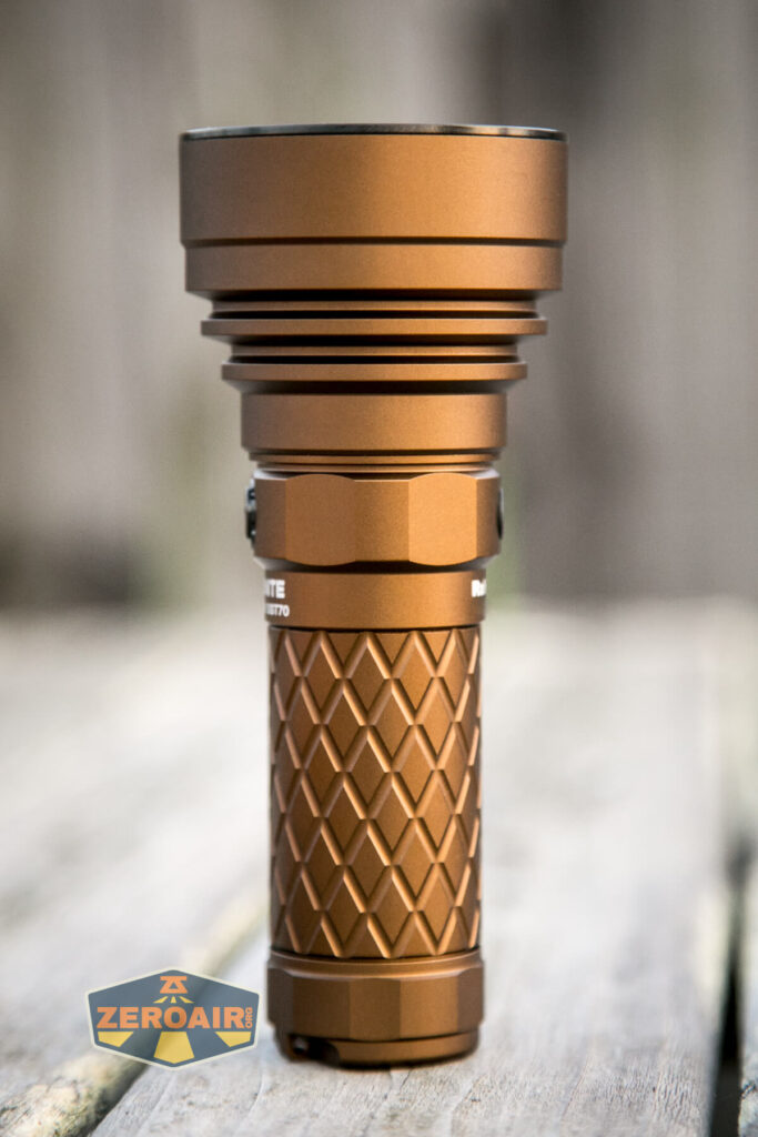 A bronze-colored flashlight with a textured grip stands upright on a wooden surface, with a blurred background and a ZeroAir logo in the lower left corner.