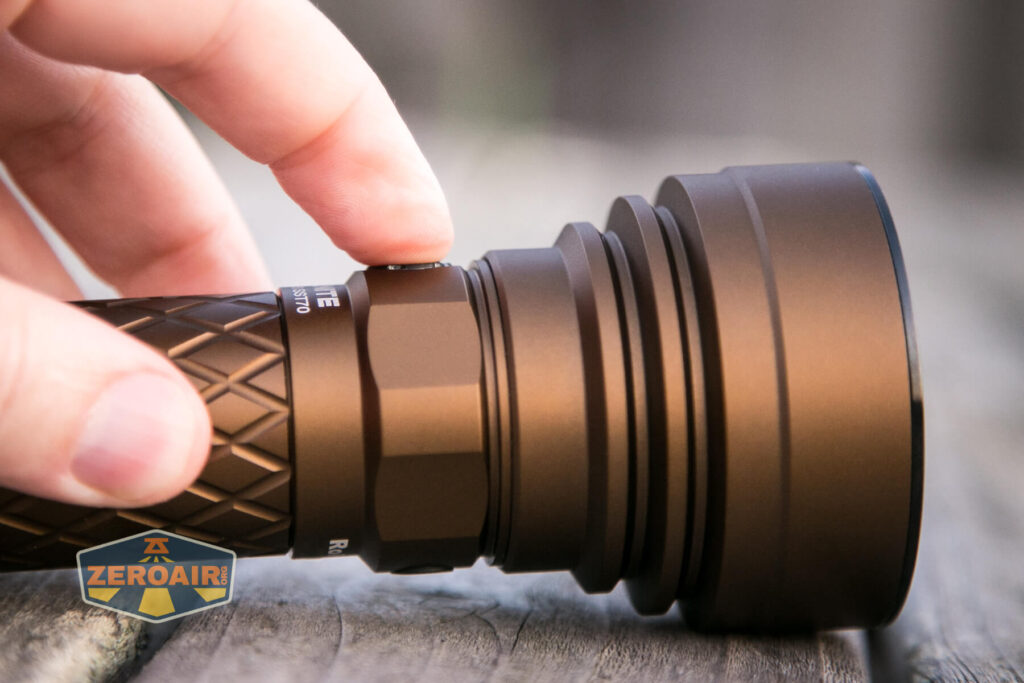 A hand is pressing the side button on a black, textured flashlight lying on a wooden surface. The flashlight has a wide head and the brand logo ZEROAIR is visible in the bottom left corner.