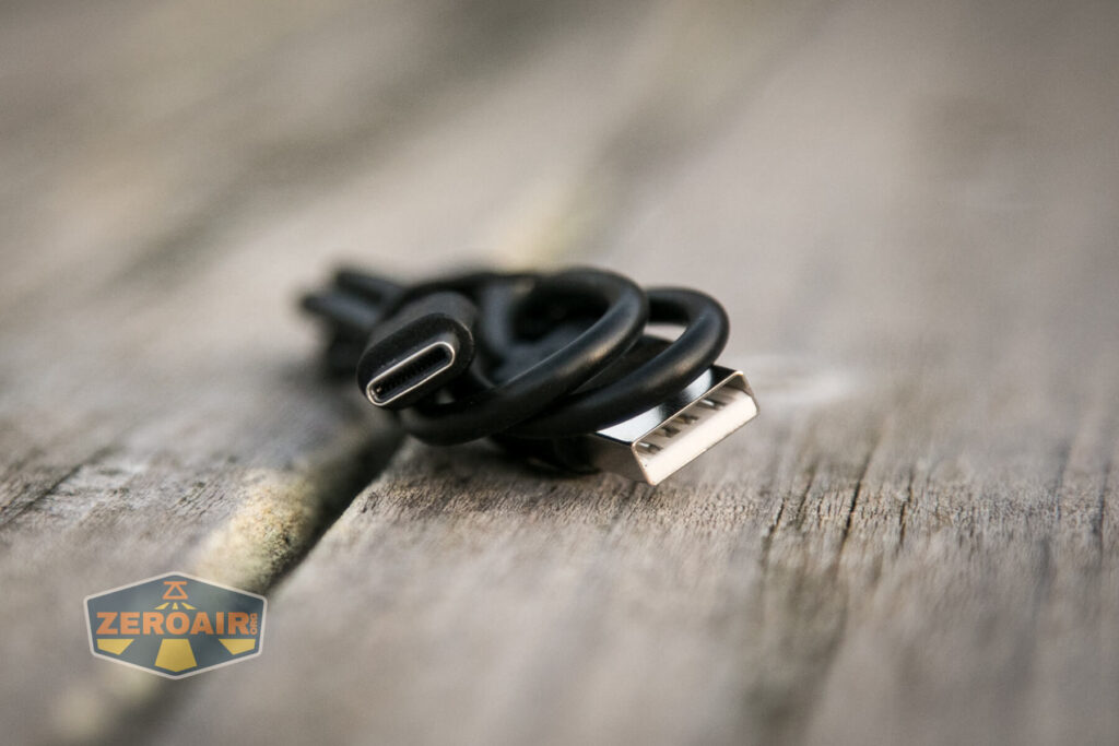 Close-up of a short black USB cable with a USB-A and USB-C connector, coiled on a weathered wooden surface. A ZEROAIR logo appears in the lower left corner.