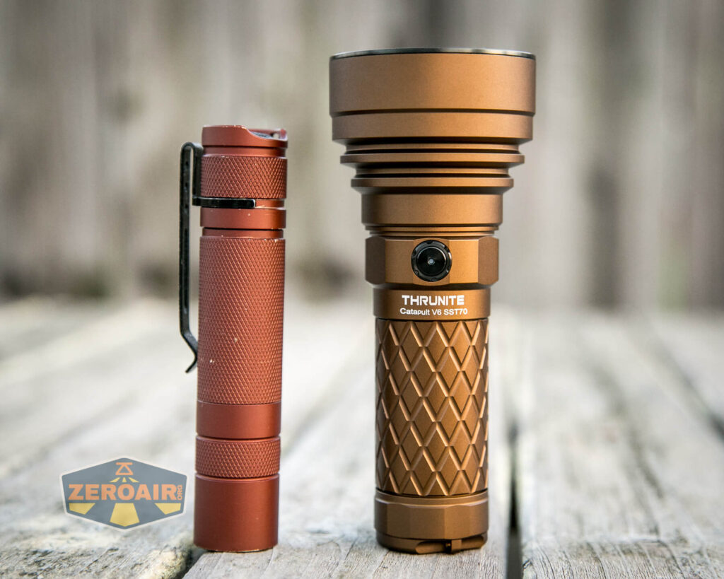 Two bronze-colored flashlights stand upright on a wooden surface. The left one is slim with a pocket clip, while the right one is larger, labeled THRUNITE, with a textured grip and a power button. A ZEROAIR logo is visible in the corner.