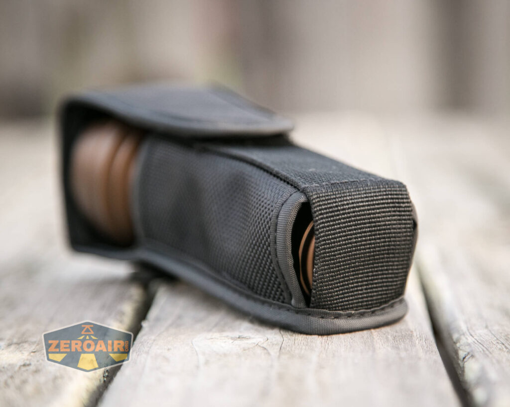 A black fabric case with a flap partially covers a cylindrical brown object, resting on a wooden surface. A logo in the corner reads “ZeroAir.”