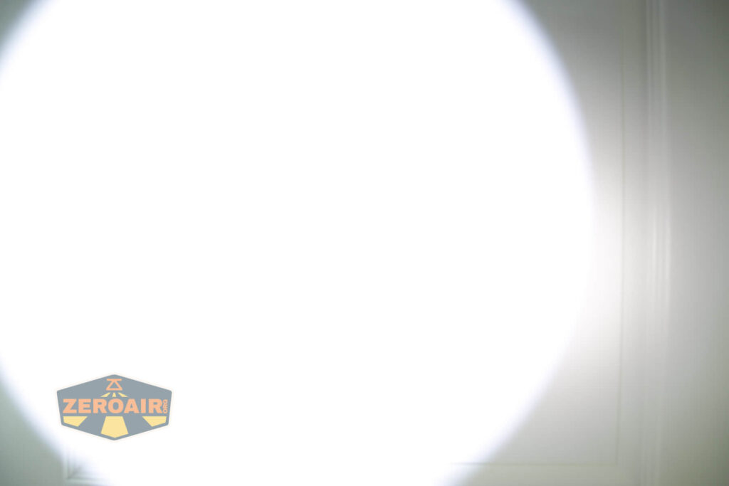 A bright white flashlight beam illuminates the center of a smooth surface, with a faint outline of a rectangular panel or door visible. The ZeroAir logo appears in the bottom left corner.