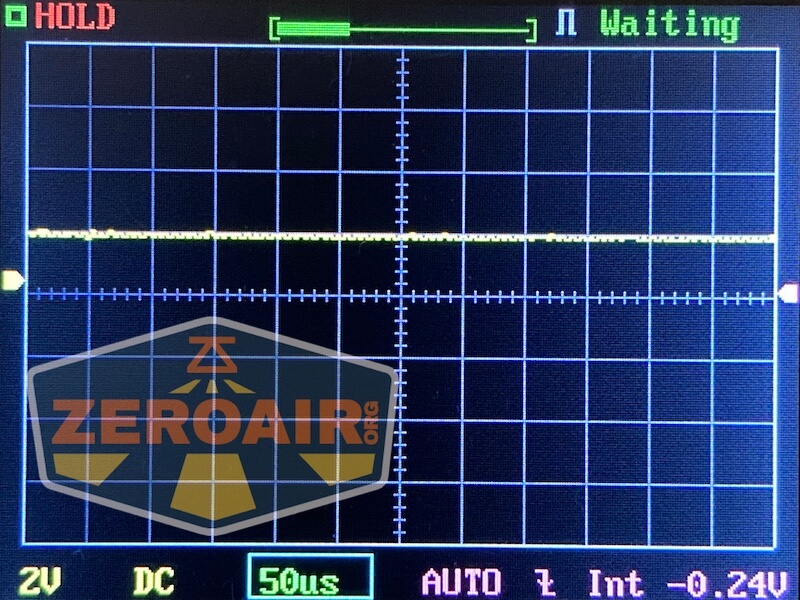 Oscilloscope screen displaying a flat yellow signal line near zero, grid lines, and measurement settings. The word Waiting appears at the top, and a large ZEROAIR watermark covers part of the screen.