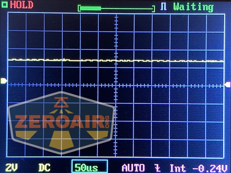 A digital oscilloscope screen shows a nearly flat yellow waveform. The display reads HOLD in red, Waiting in green, and various measurement settings, including 2V, DC, 50µs, AUTO, 0.24V. A ZEROAIR watermark is visible.