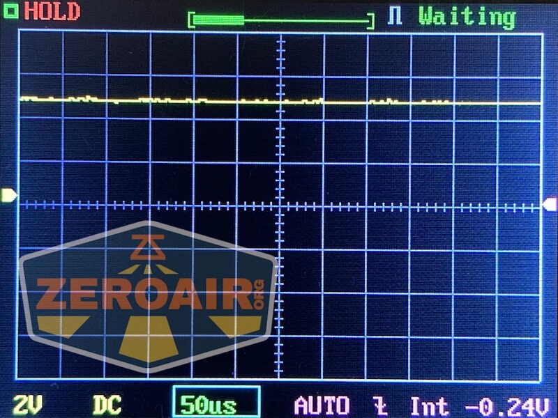 A digital oscilloscope screen displays a flat yellow signal line near the top. The words HOLD and Waiting are visible, along with voltage and time settings. A watermark reading ZEROAIR covers part of the lower left corner.
