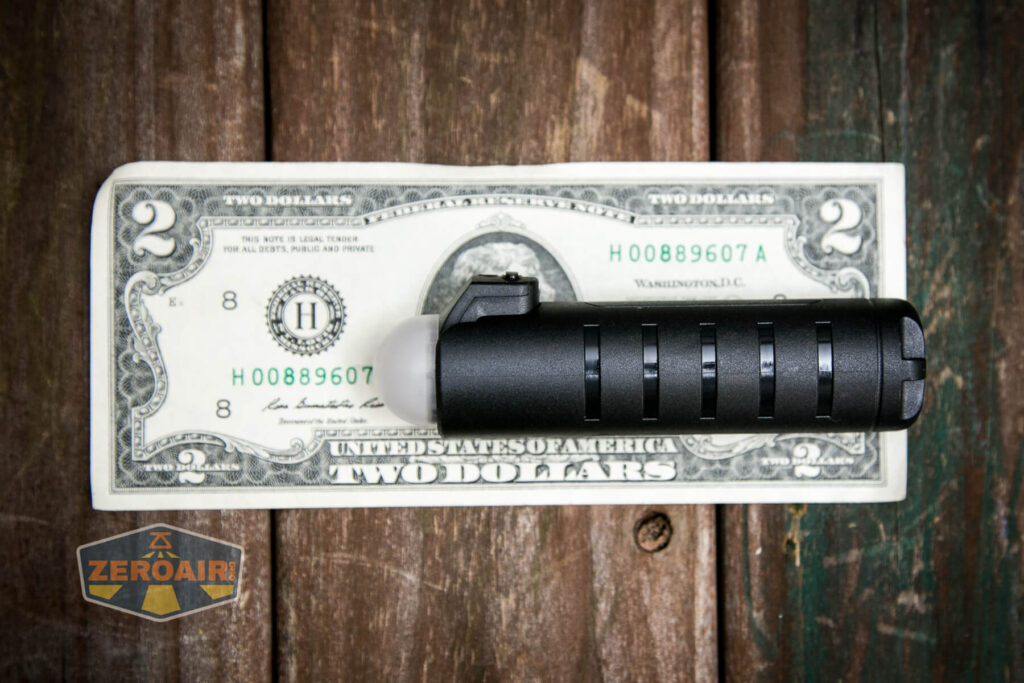 A black cylindrical flashlight with grooved sides is placed on top of a two-dollar bill on a wooden surface. A ZeroAir logo appears in the bottom left corner of the image.