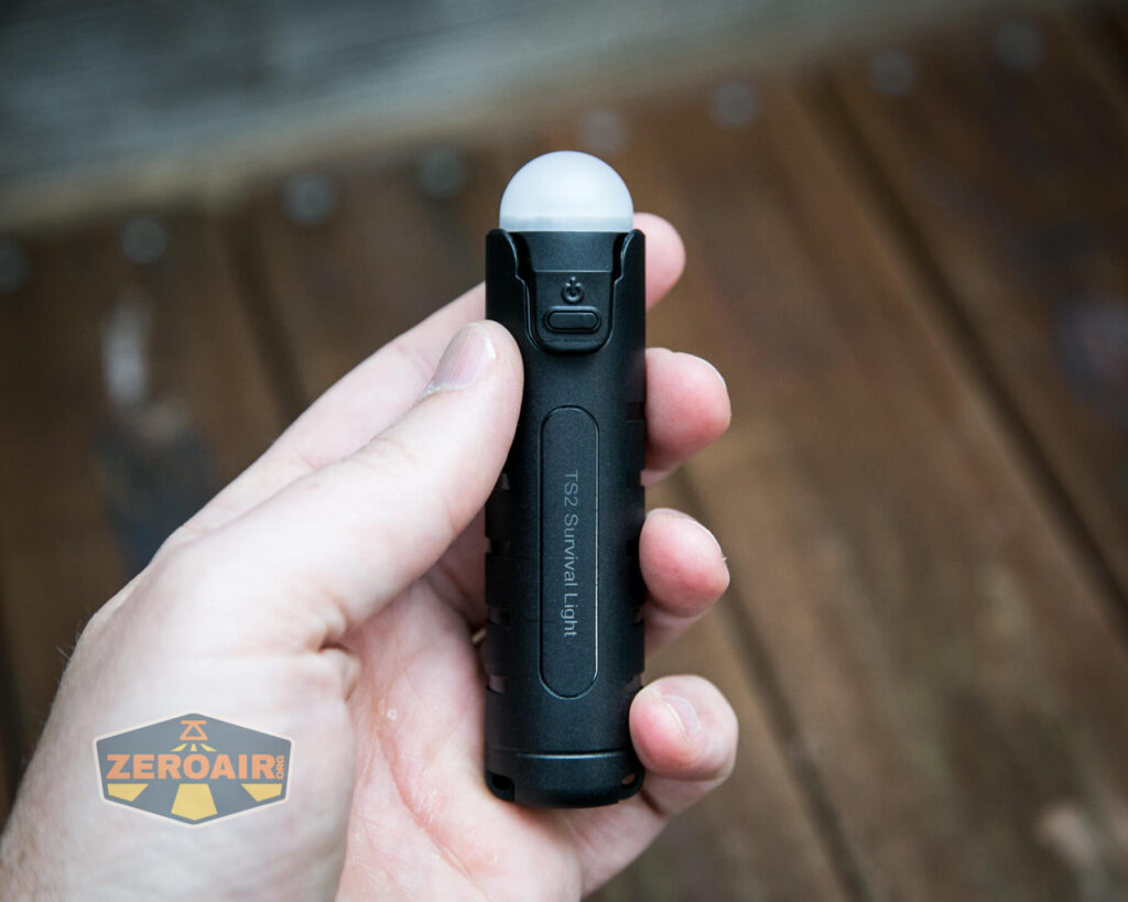 A hand holds a compact, black flashlight with a dome-shaped white diffuser on top. “1921 SIGNALING LIGHT” is printed along the side. The ZeroAir logo appears in the lower left corner. The background is wooden planks.