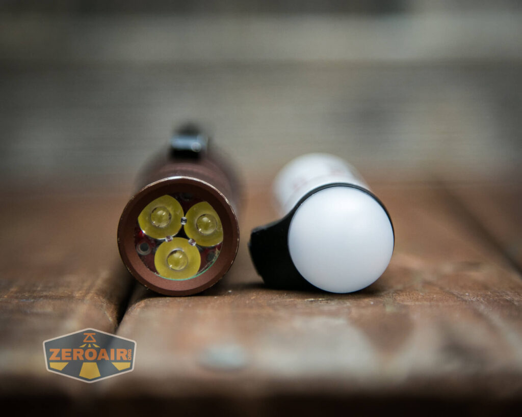 A close-up of two flashlights lying on a wooden surface; one shows three LED bulbs, and the other has a white diffuser cap. A ZeroAir logo is visible in the lower left corner.