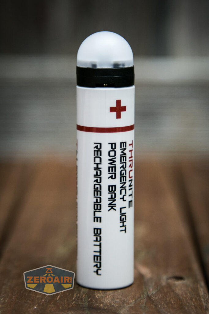 A cylindrical white device with a rounded top, featuring a red cross and labeled “ThruNite Emergency Light Power Bank Rechargeable Battery,” placed upright on a wooden surface. A ZeroAir logo is visible in the corner.