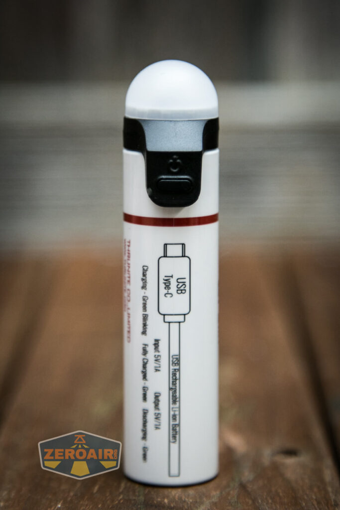 A white cylindrical device with a rounded top and a black button, featuring a diagram of a USB Type-C charging cable and charging specifications printed on the side.