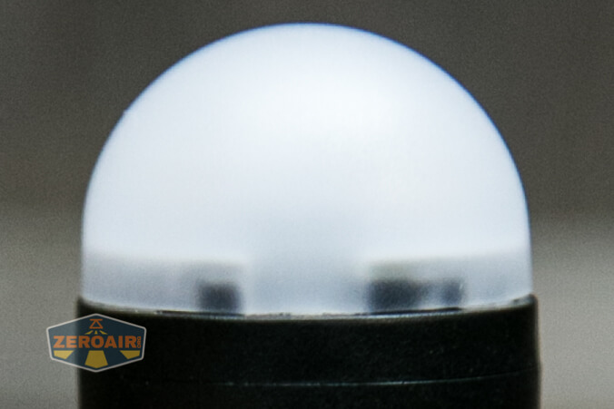 A close-up of a round, frosted white dome light diffuser on top of a black cylindrical base. A small ZeroAir logo appears in the lower left corner.