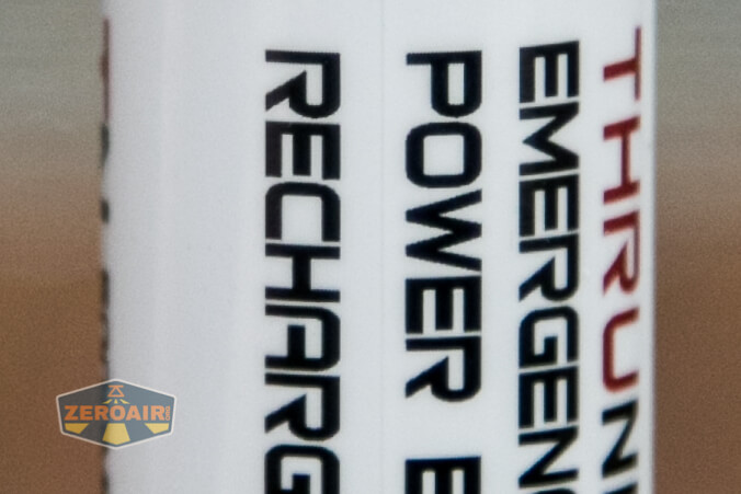 Close-up of a cylindrical object showing partially visible text in bold letters, including EMERGENCY, POWER, RECHARGE, and a logo in the lower left corner that reads ZEROAIR.