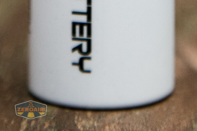 A partial view of a white cylindrical object with black, vertically oriented text is shown. The object sits on a rough surface. The ZeroAir logo is visible in the lower left corner.