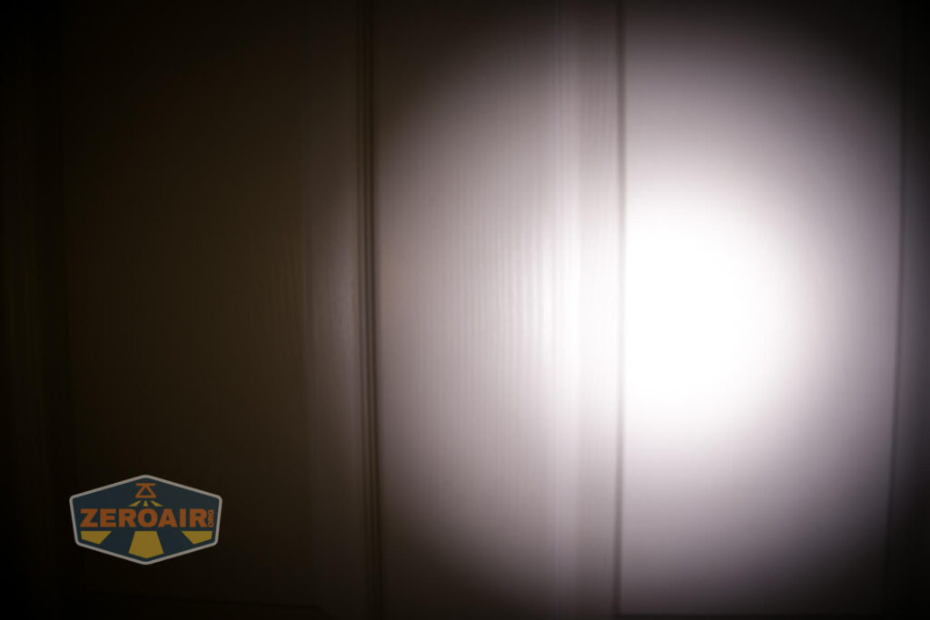 A close-up of a door illuminated by a flashlight beam, creating a circular bright spot in the center. The ZeroAir logo is in the lower left corner.