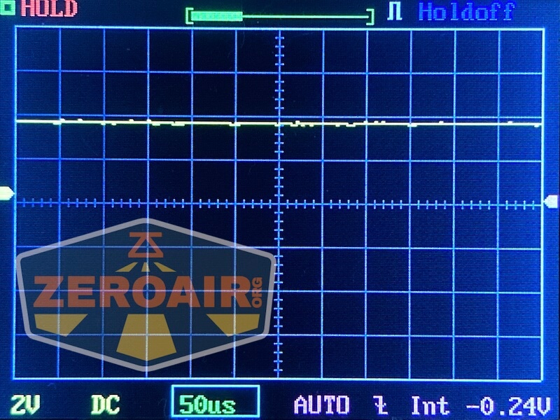 A digital oscilloscope screen displays a mostly flat yellow waveform near zero volts. The settings show 2V/div, 50 microseconds/div, DC coupling, and a measured value of -0.24V. A ZEROAIR logo covers part of the screen.