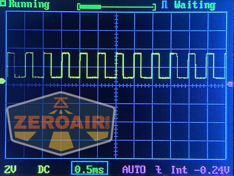 An oscilloscope screen displays a square wave signal with a yellow trace. The settings show 2V per division vertically and 0.5ms per division horizontally. The screen also shows “ZEROAIR” watermark.