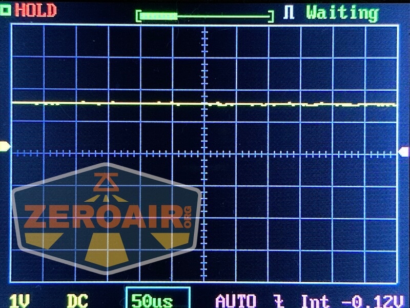 Oscilloscope screen displaying a mostly flat yellow signal trace on a black grid, with Waiting and HOLD indicators, and measurement settings including 1V DC and 50μs. A large ZEROAIR watermark is visible.