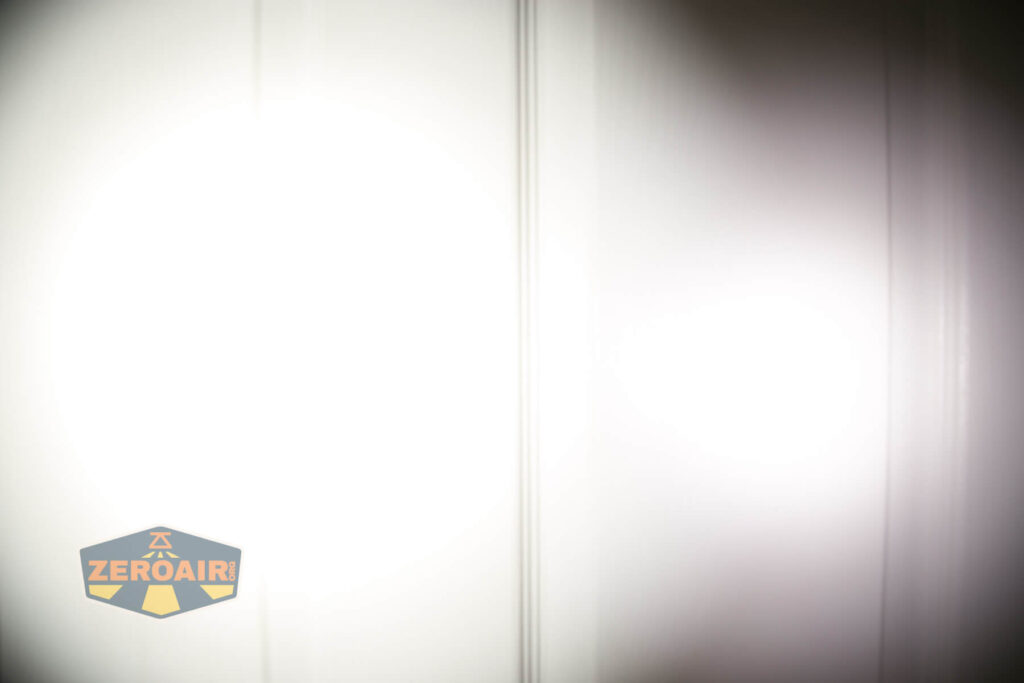 A bright flashlight beam shines on a white door, creating a circular pattern of light with a faded edge. The ZeroAir logo appears in the bottom left corner of the image.