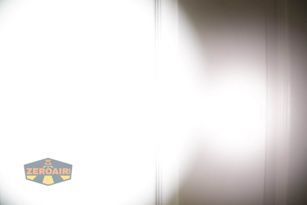 A bright white light shines on a flat surface with faint vertical lines. The left side of the image is illuminated, while the right side displays a shadow. A ZeroAir logo appears in the bottom left corner.