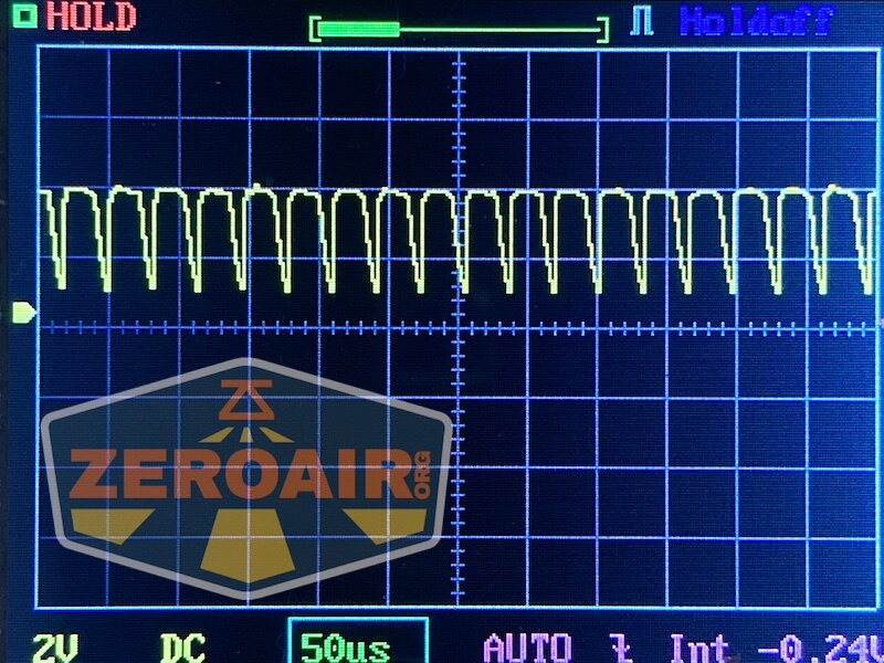 An oscilloscope screen displays a periodic waveform with sharp peaks and valleys. The settings show 2V DC and a time division of 50 microseconds. The ZEROAIR logo is overlaid in the lower left corner.