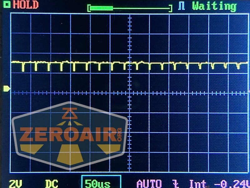 An oscilloscope display shows a waveform with small, regular peaks on a grid. The screen reads HOLD, Waiting, 2V DC, 50µs, and AUTO at the bottom. A ZEROAIR logo is partially visible.