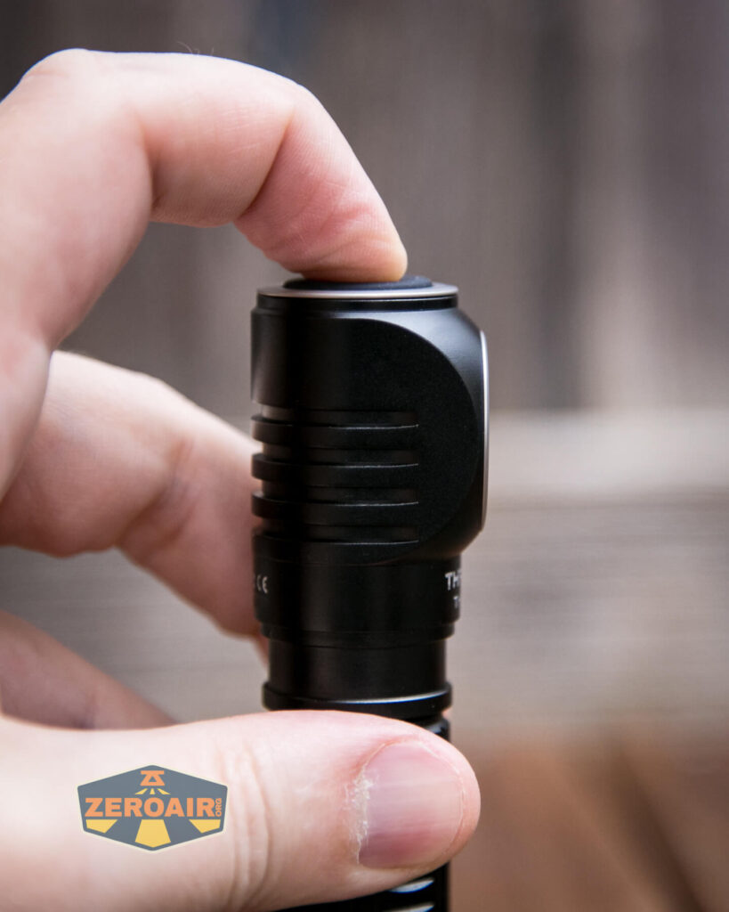 A hand presses the button on the end of a black flashlight. The flashlight is held upright, with a visible logo reading ZEROAIR! in the bottom left corner. The background is out of focus.