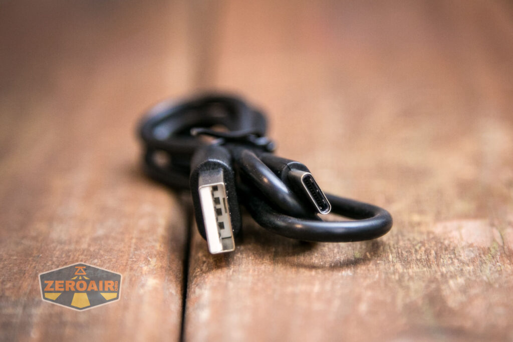 A black USB cable with a USB-A connector on one end and a USB-C connector on the other is coiled on a wooden surface, with a ZeroAir logo visible in the lower left corner.