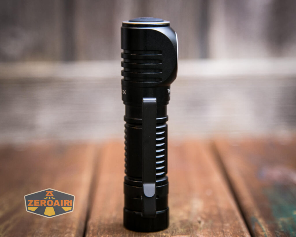 A black, cylindrical flashlight stands upright on a wooden surface with a blurred background. The flashlight has a metallic clip and ribbed grip. A ZeroAir logo appears in the lower left corner.