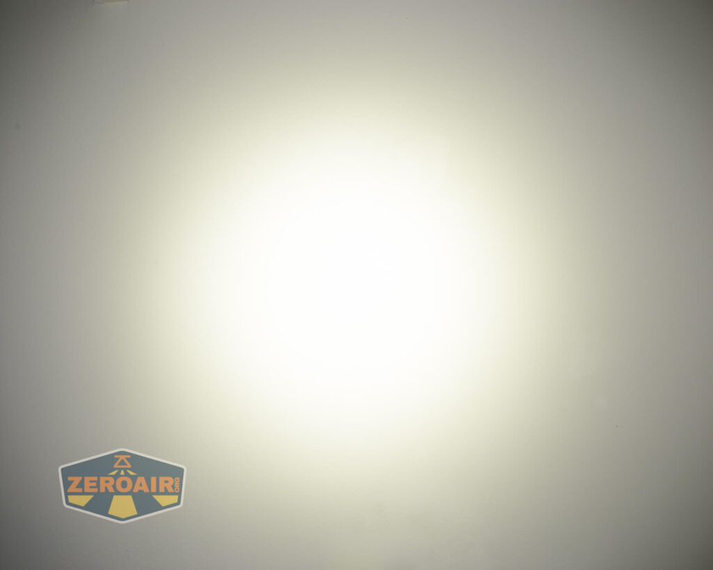 A white wall illuminated by a bright, circular beam of light at the center. The bottom left corner features a yellow and gray ZEROAIR logo.