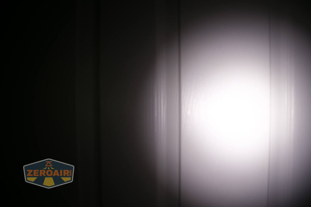 A bright flashlight beam shines on a white paneled surface in a dark room. The logo ZEROAIR is visible in the lower left corner.