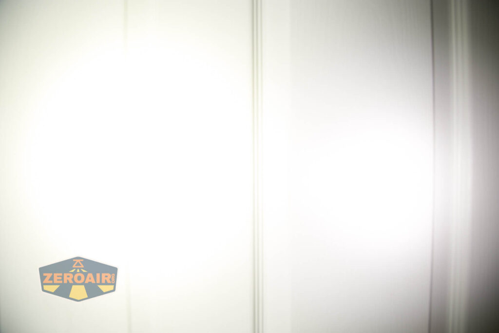 A white door with subtle vertical panel lines is brightly illuminated, making most surfaces appear washed out. A logo with the text ZEROAIR is in the lower left corner.