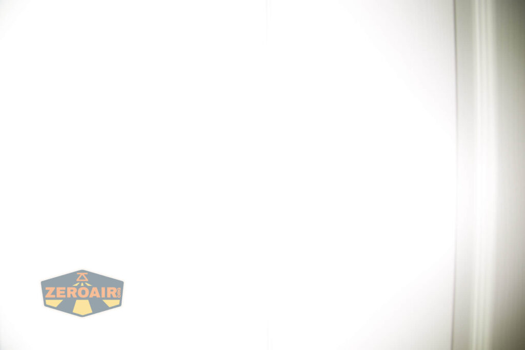 A mostly white, overexposed image with faint vertical lines on the right side. The lower left corner features a hexagonal logo with the text ZEROAIR in yellow on a blue background.