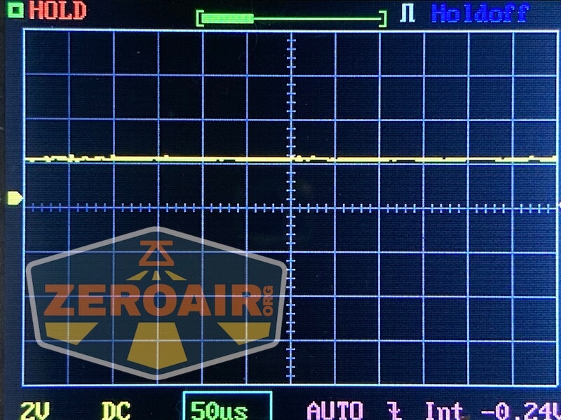 A digital oscilloscope display shows a mostly flat yellow signal trace centered on the horizontal axis. The screen has grid lines and various measurement indicators. The ZEROAIR logo is overlaid in the bottom left corner.