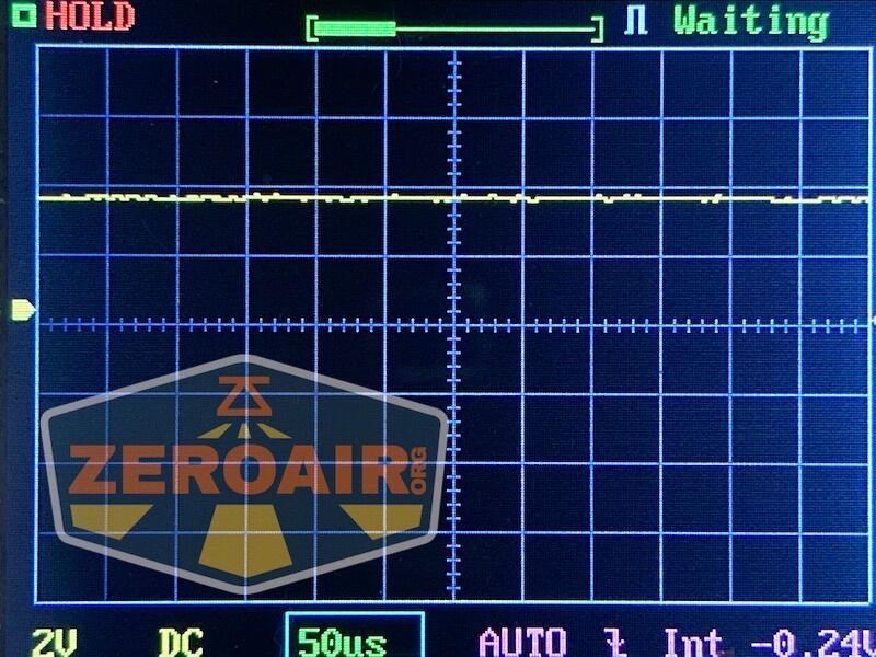 Oscilloscope screen displaying a flat yellow waveform on a grid, with HOLD and Waiting indicators. The voltage is set to 2V per division, time base to 50 microseconds. ZEROAIR.org logo is overlaid.