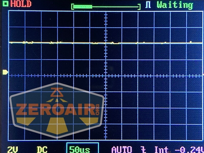 A digital oscilloscope screen displays a flat yellow waveform on a grid. The words “HOLD” and “Waiting” appear at the top, and a ZEROAIR.org logo is visible in the bottom left corner.