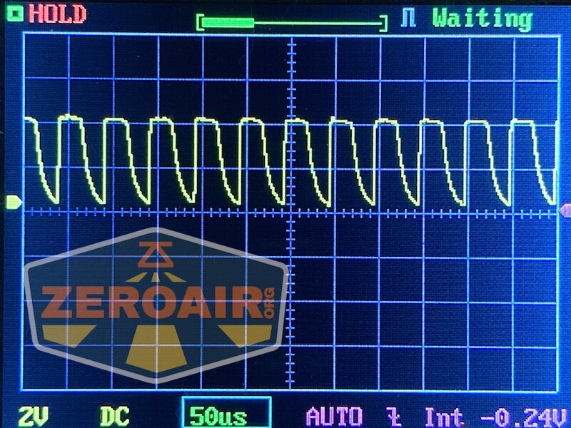An oscilloscope screen displays a repeating sawtooth waveform. The settings show 2V per division vertically and 50 microseconds per division horizontally. The screen also shows the words HOLD and Waiting.