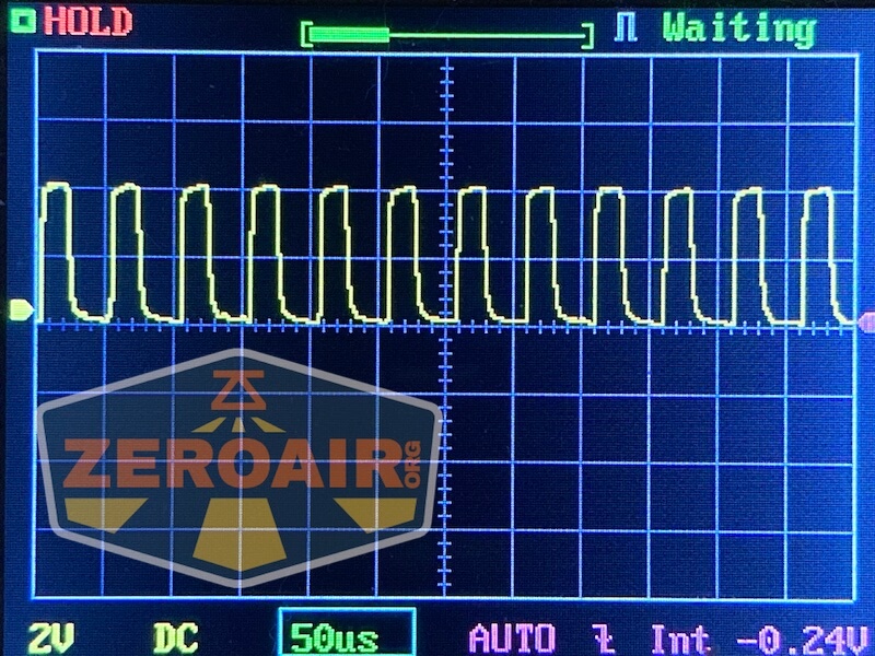 Oscilloscope screen displays a repeating square waveform signal. The settings show 2V per division, 50 microseconds per division, and a DC coupling. The screen also has the ZEROAIR.org logo partially visible.