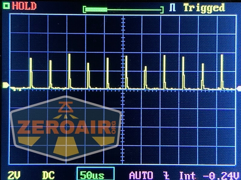 A digital oscilloscope screen displays a repetitive pulse waveform. The settings along the bottom show 2V per division, DC coupling, and 50 microseconds per division. HOLD and Triggered are indicated.