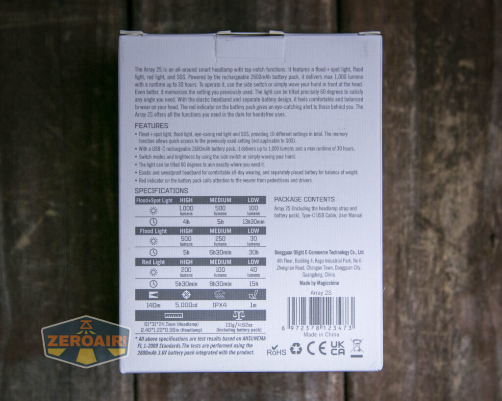 A close-up of the back of a product box on a wooden surface, showing detailed text with features, specifications, and package contents for a headlamp, including light output and runtime information. A ZeroAir logo sticker is visible.