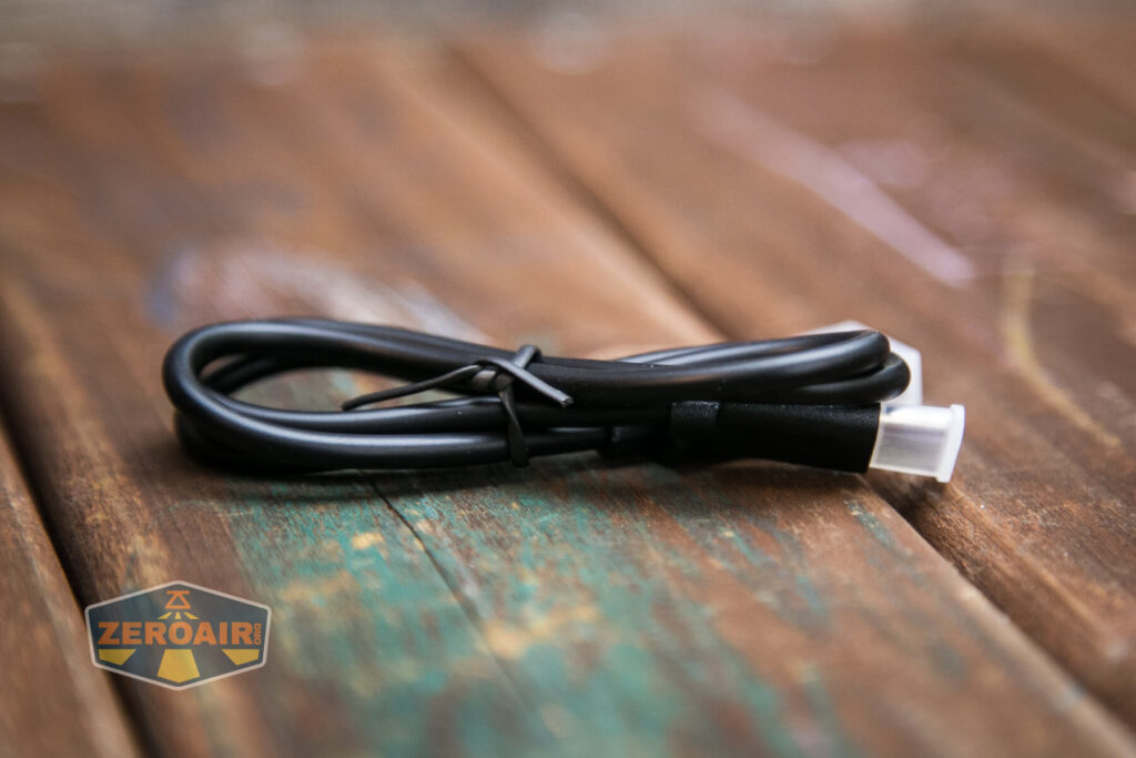 A black USB cable is coiled and secured with a twist tie, resting on a weathered wooden surface. A small ZeroAir logo appears in the bottom left corner.