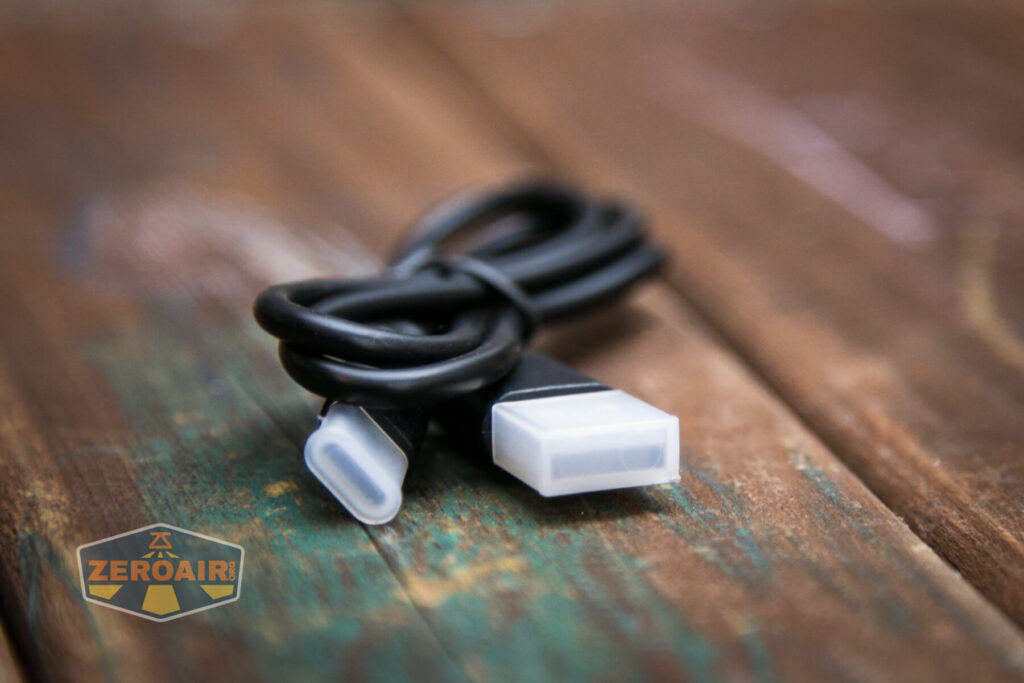 A close-up of a black USB cable with white connectors lying on a worn wooden surface. A ZEROAIR logo is visible in the bottom left corner.