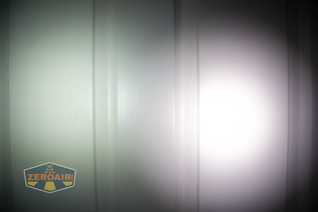 A white flashlight beam shines on a white paneled surface, creating a bright circular spot in the center with soft gradient edges. The ZeroAir logo is visible in the lower left corner.