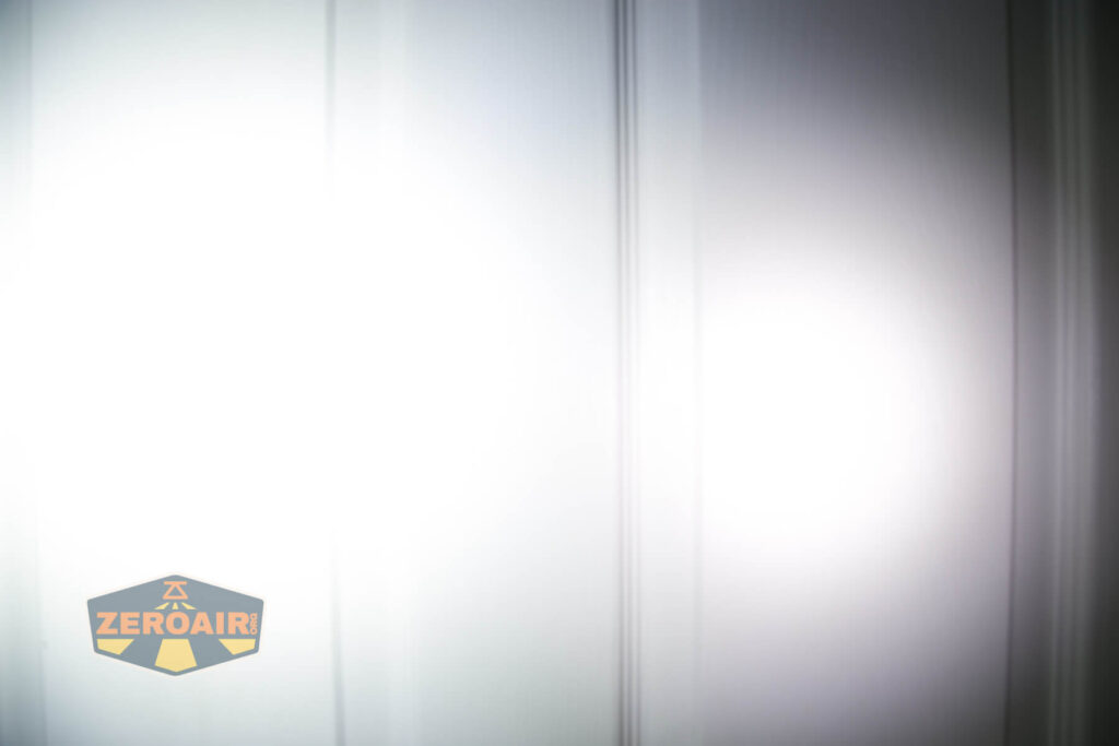 A bright white light shines on a white paneled door, creating a circular illuminated area. The ZeroAir logo appears in the lower left corner of the image.