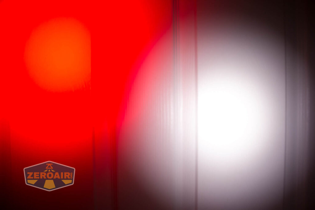 A bright red light and a bright white light are projected onto a vertical ridged surface. A ZeroAir logo is visible in the bottom left corner of the image.