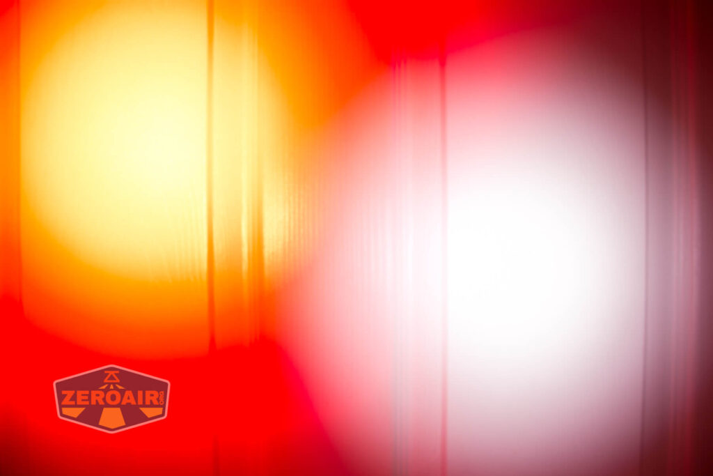 Abstract image showing large, blurred circles of red, orange, and white light. Vertical lines run through the image, and a logo with the text ZEROAIR appears in the bottom left corner.