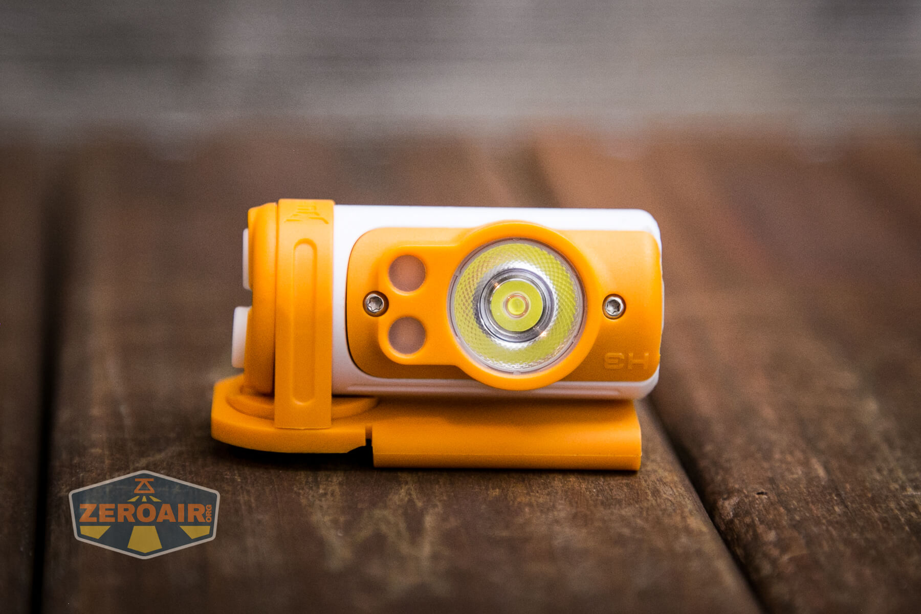 A compact orange and white flashlight with a single LED lens sits on a wooden surface. A logo reading ZEROAIR is visible in the lower left corner of the image.